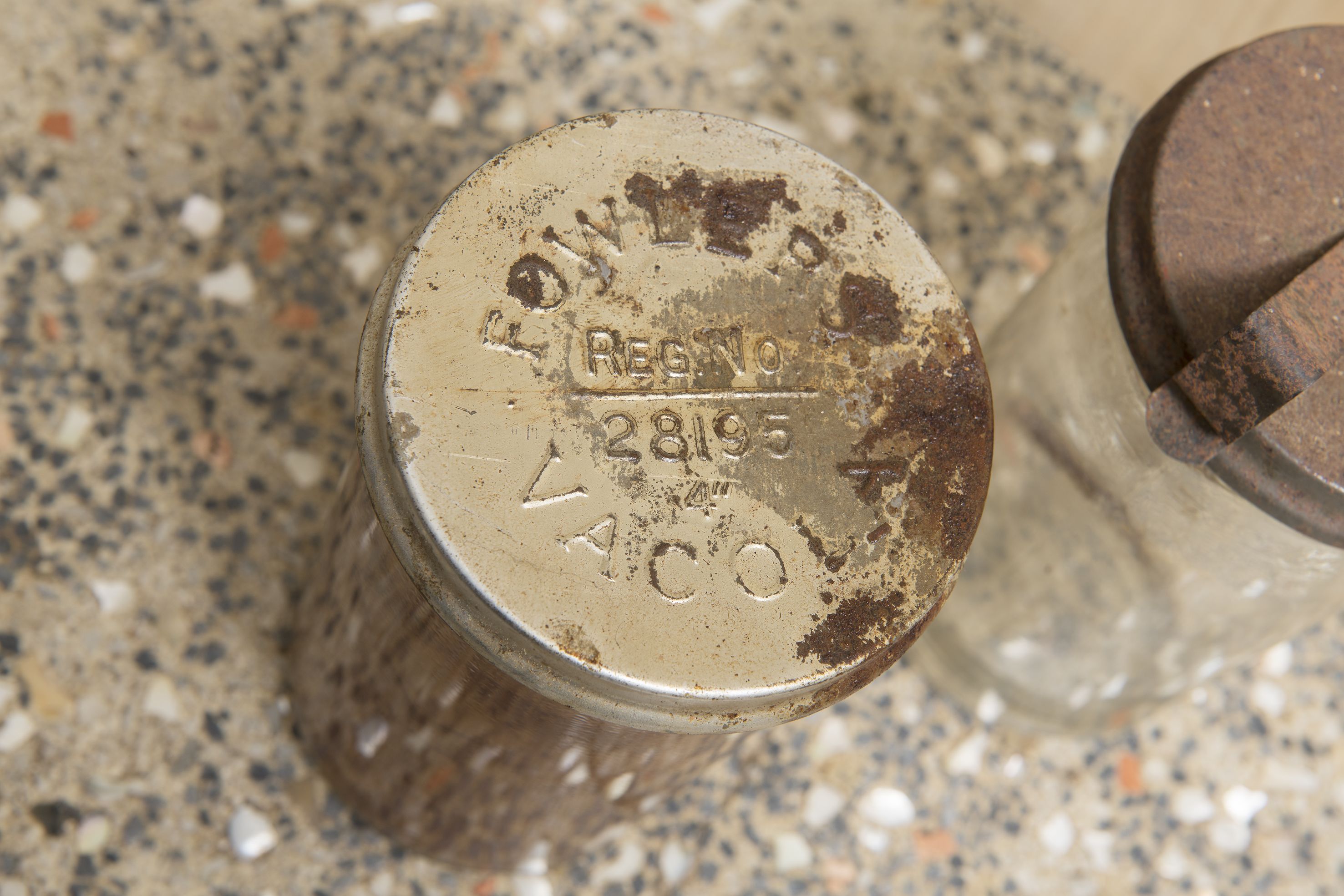 A close up of a tarnished Fowlers Vacola lid, looking down on a stone benchtop.