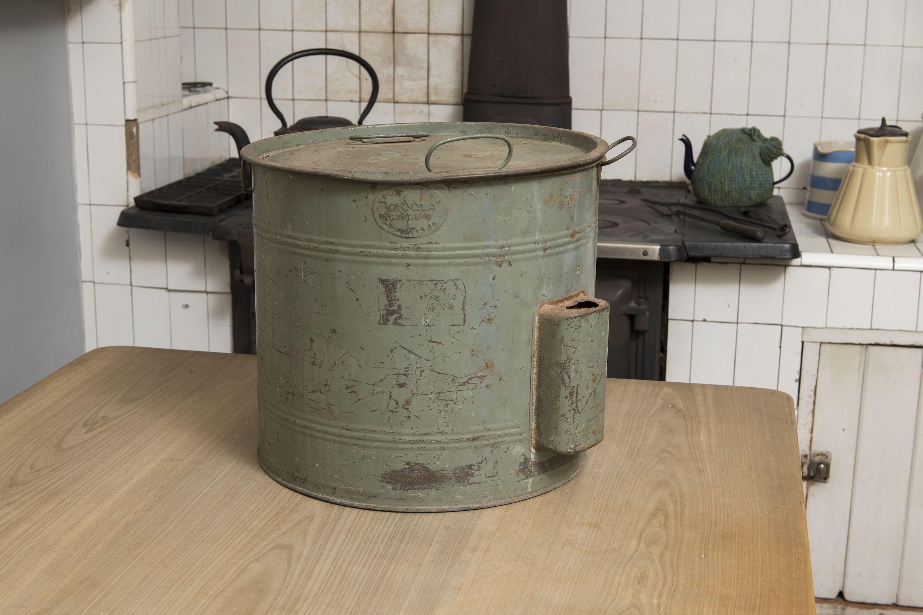 A green metal preserving pan sitting on a wooden table.
